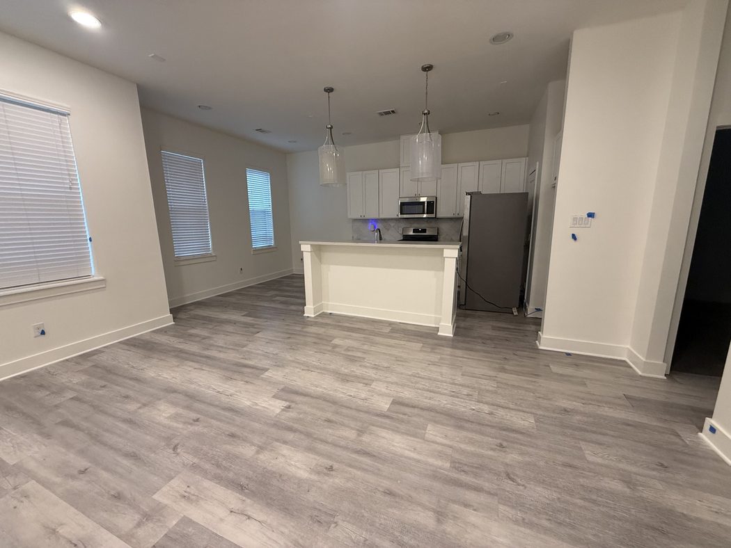 Kitchen with a white island, pendant lights and gray plank floors after a move-out clean