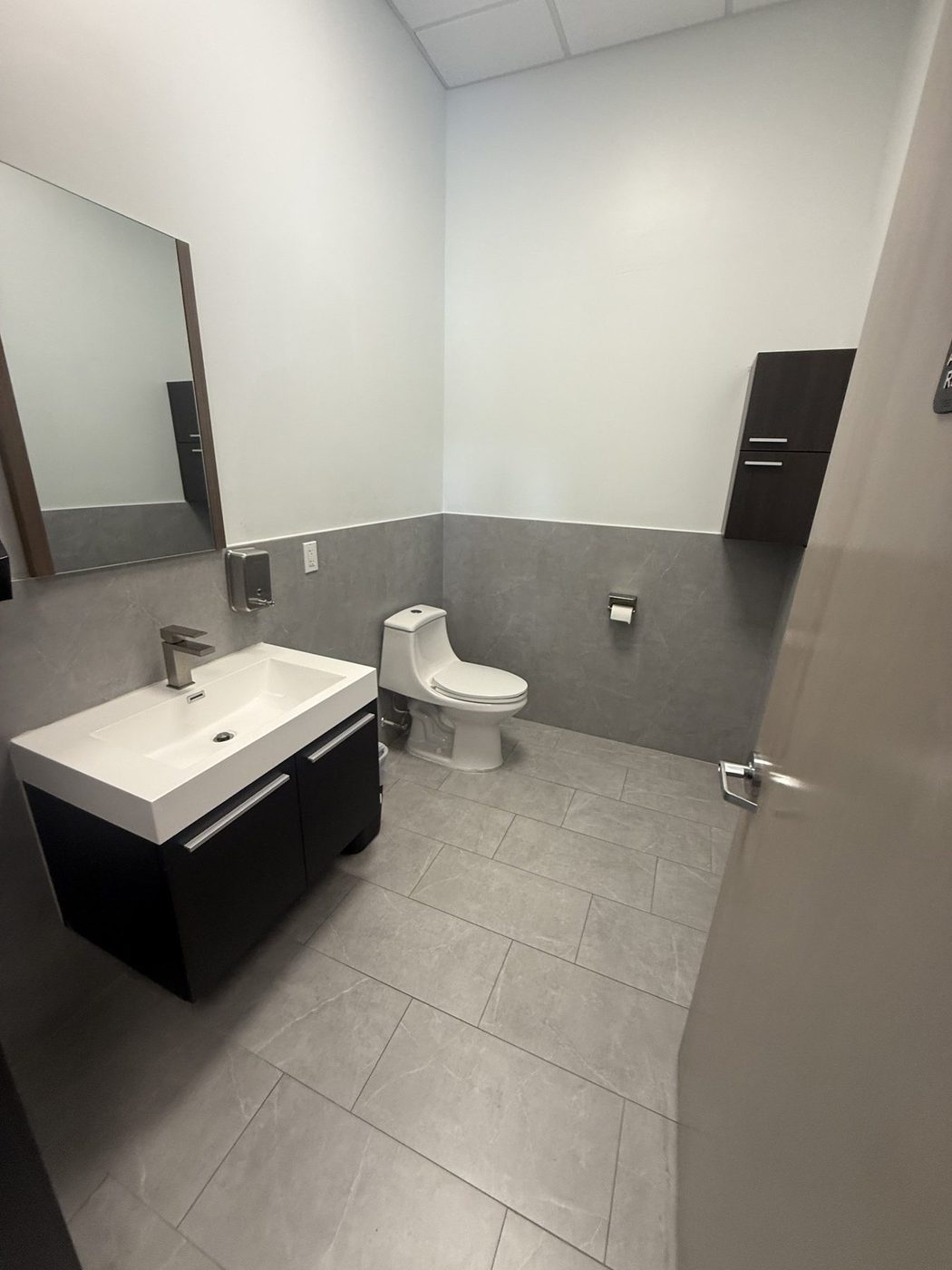 Clean single-occupancy office restroom with wall-mounted vanity and gray tile