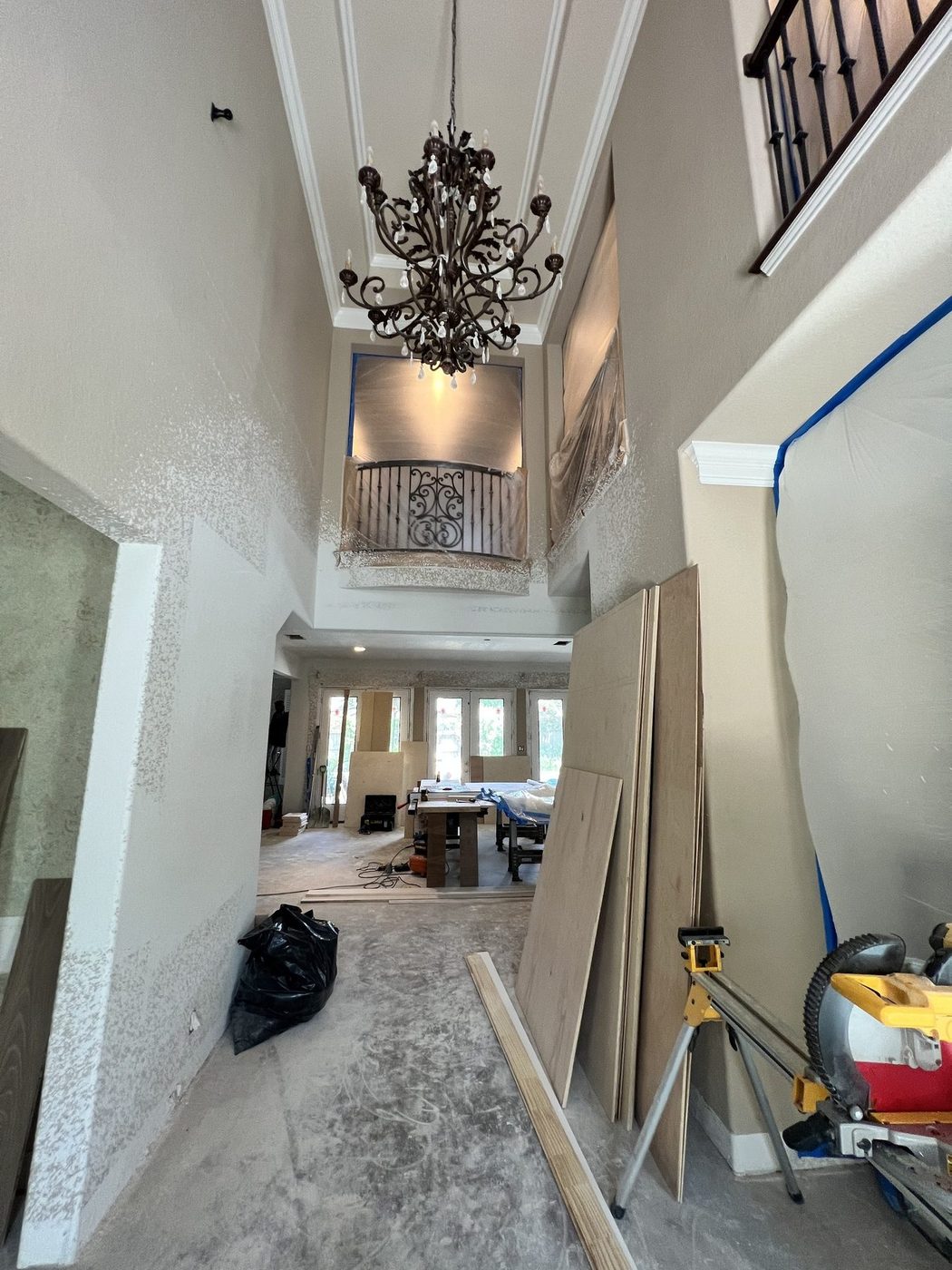 Two-story foyer during construction with debris bags, drywall sheets, lumber and a saw on a dusty floor